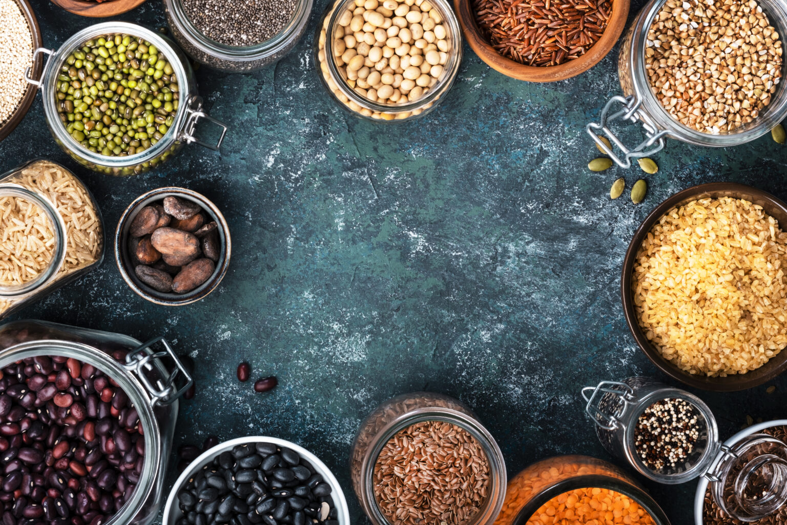 Various organic superfoods, beans, grains, cereals, legumes, seeds in reusable cans and jars. Copy space top view. Blue background